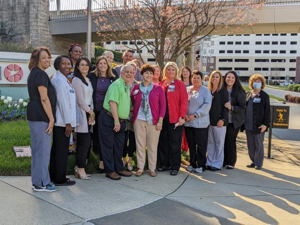 Team of hospital workers and medical personnel pose together outside hospital