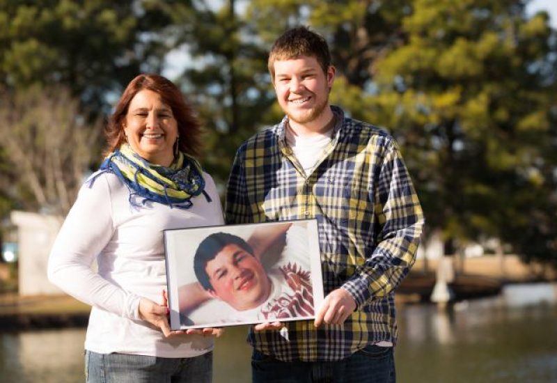 Donor mom and son holds photo of other son while next to a lake